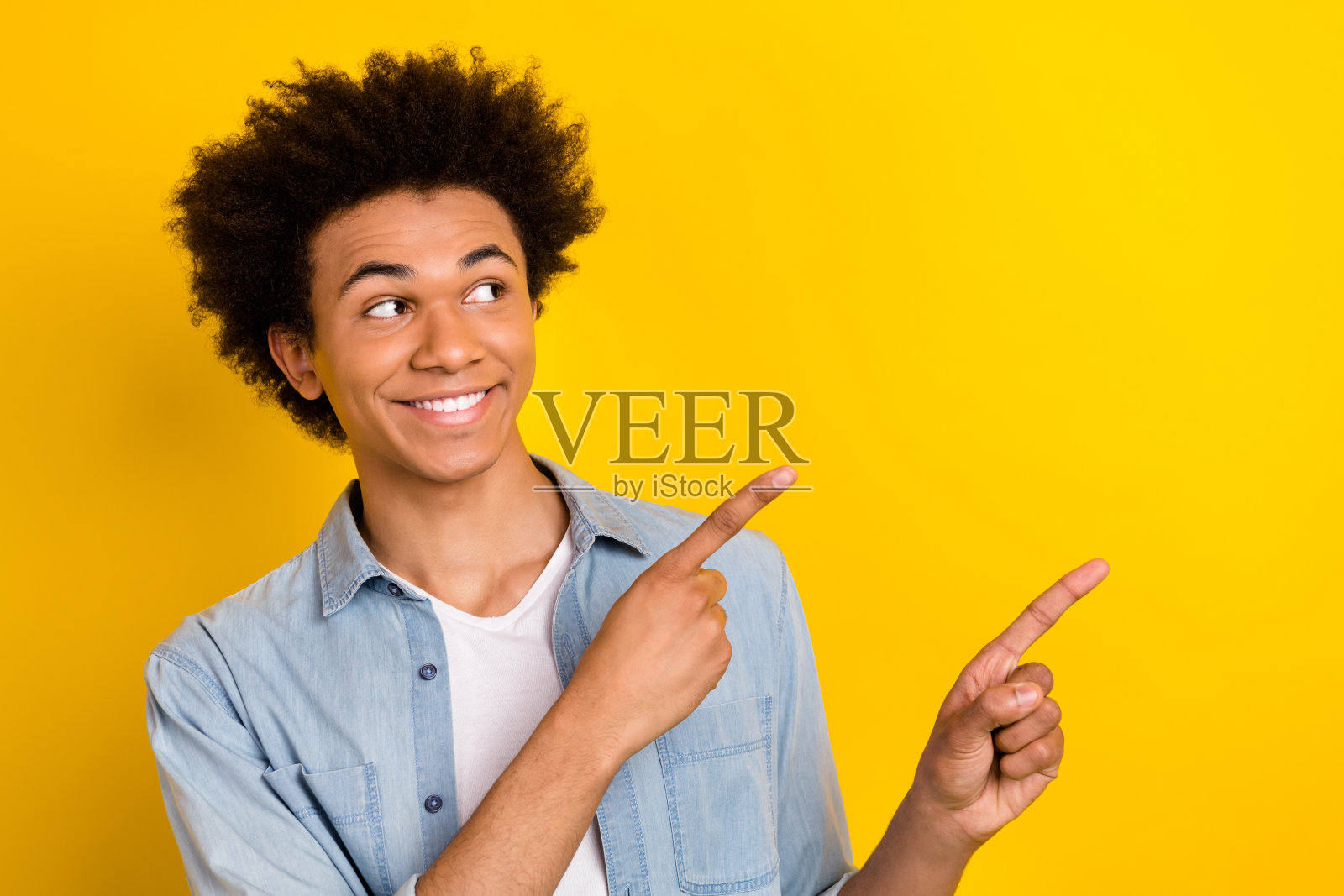 兴奋而梦幻的男子穿着牛仔衬衫,双手指向空旷的空间,背景为黄色。照片摄影图片