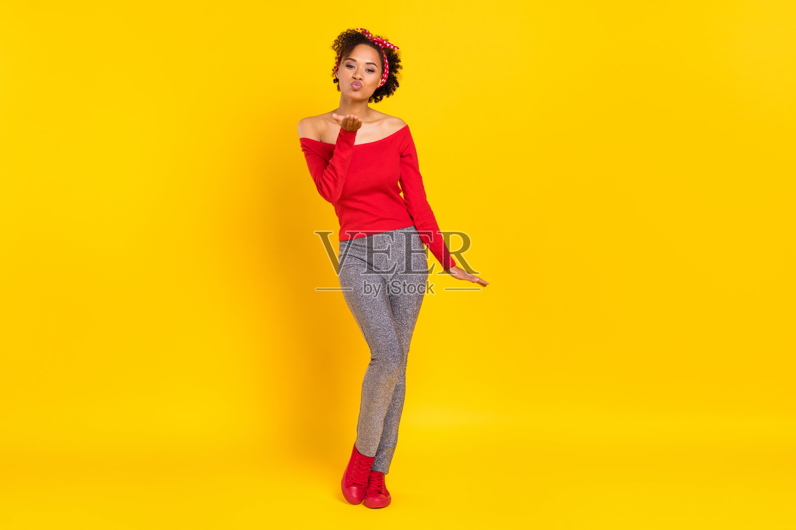 穿着复古风格服装、闪亮裤子的浪漫调皮女士在黄色背景下摆出送空气吻的姿势。照片摄影图片