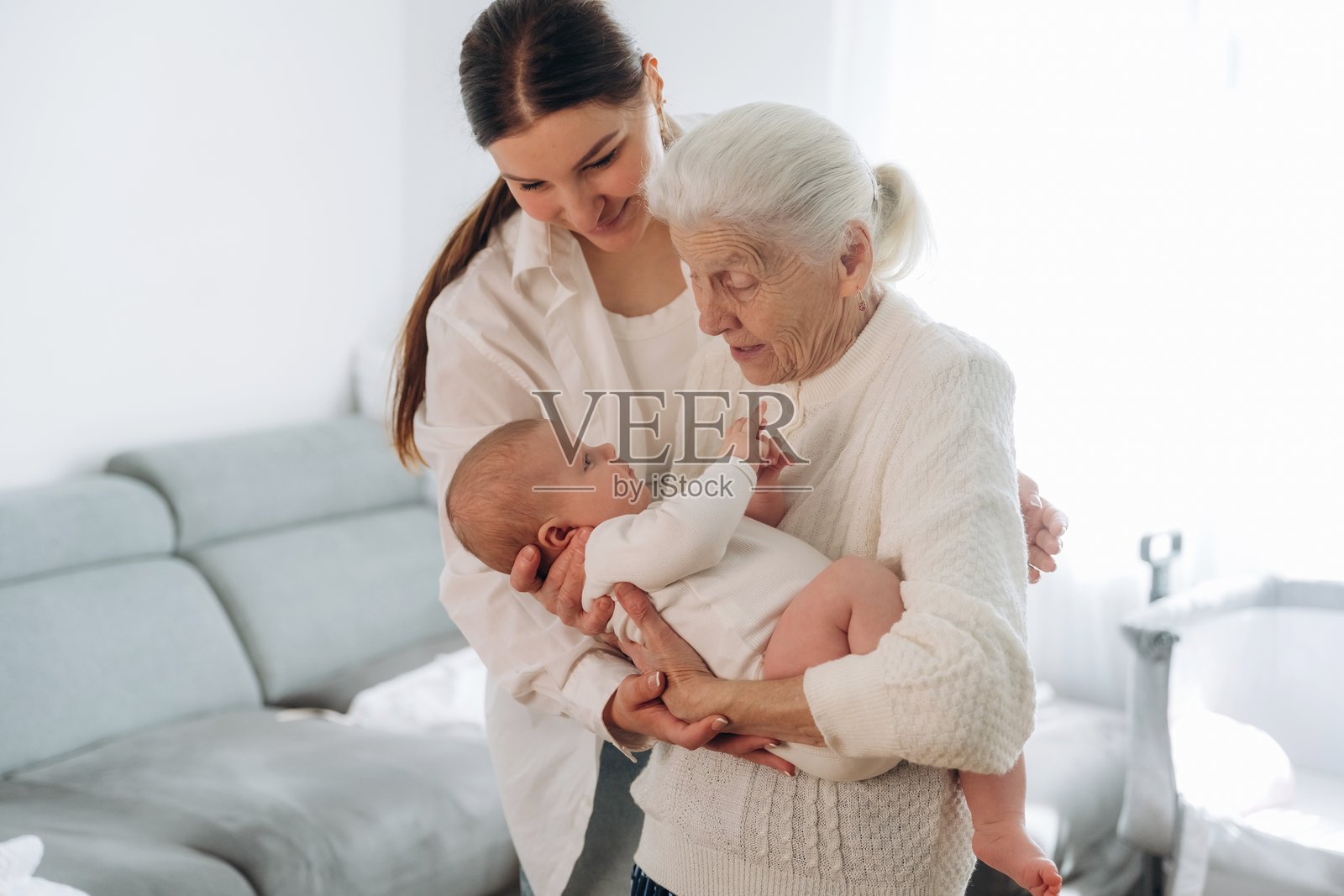 愉快的面部表情。母亲、祖母和小婴儿在室内的怀抱中。照片摄影图片