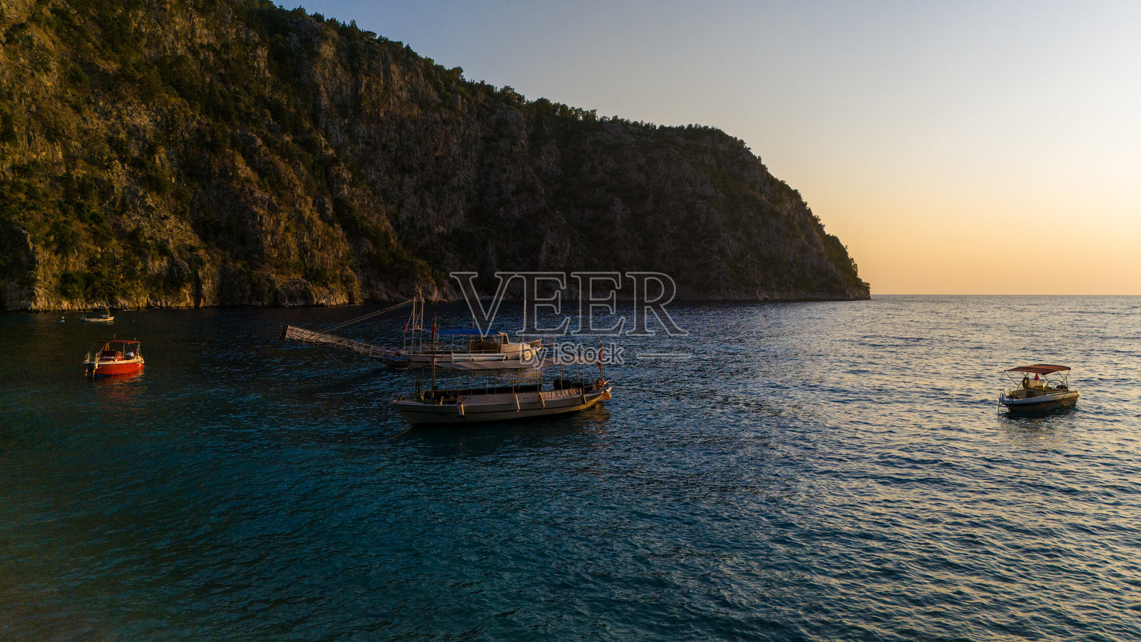 航拍无人机镜头捕捉到一艘船在日落时分平静水面上航行。照片摄影图片