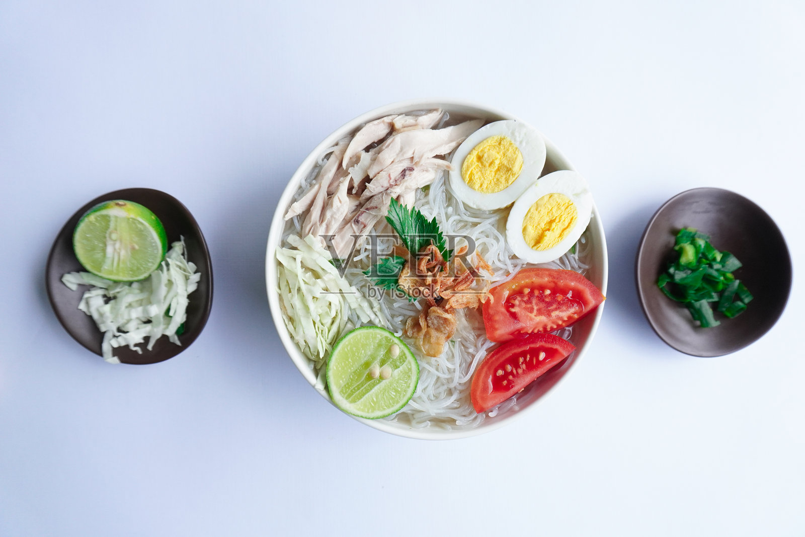 清汤鸡肉面是印尼菜,由米饭、鸡肉高汤、 shredded chicken、煮鸡蛋、米饭、卷心菜、粉丝、西红柿、芹菜和青柠组成。照片摄影图片