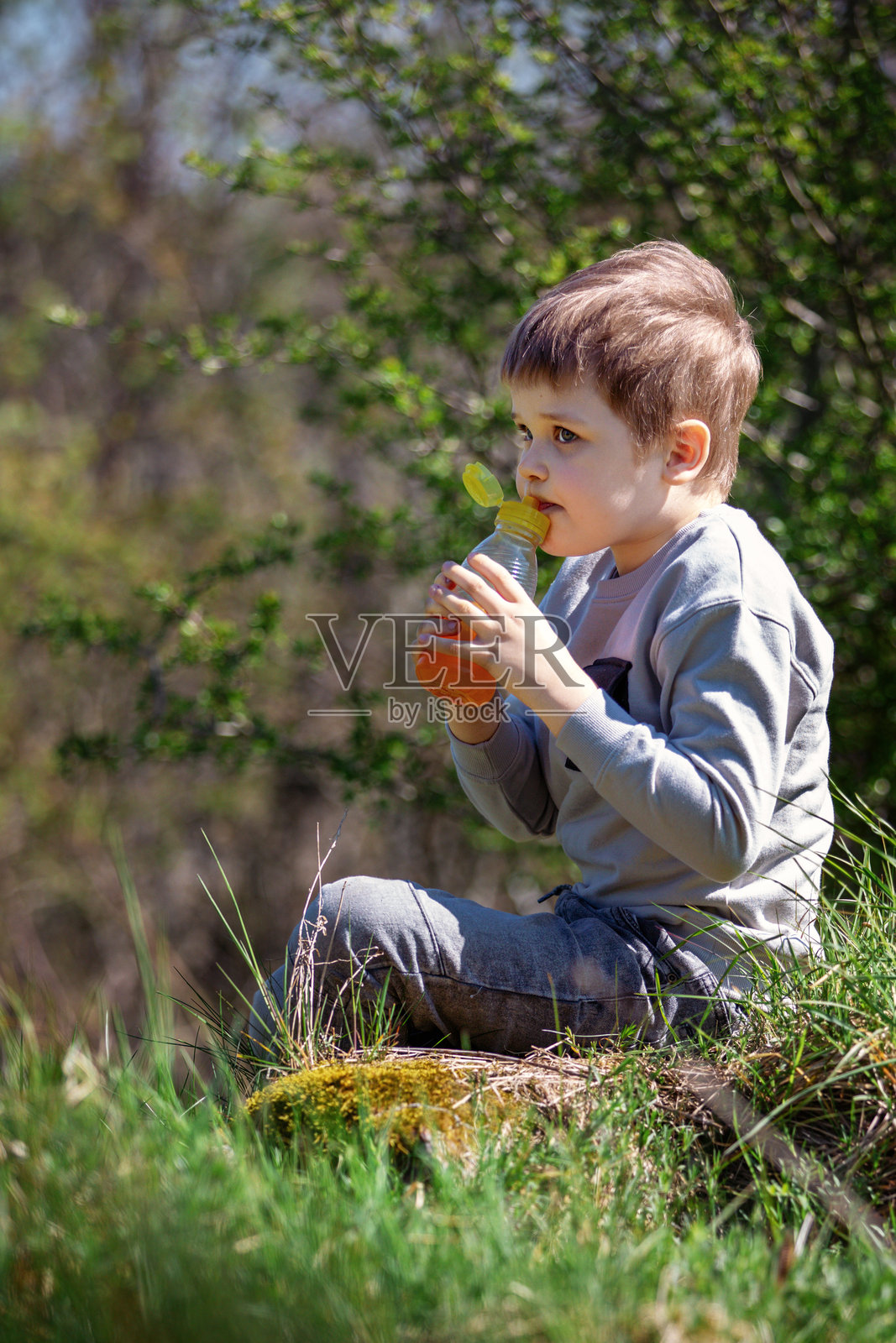 一个小男孩坐在草地上品尝橙汁照片摄影图片