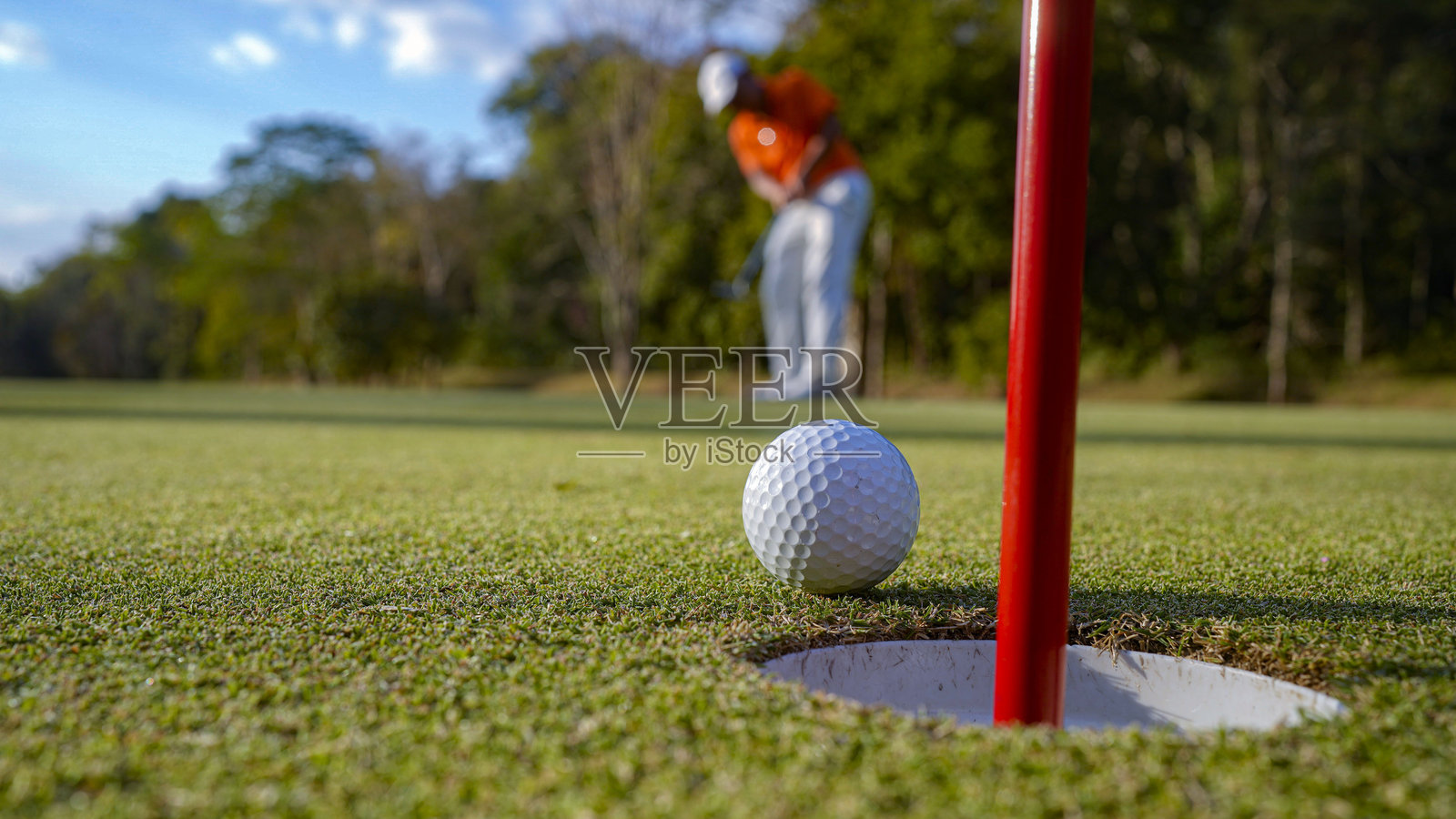 模糊的高尔夫球手在果岭上推杆,夕阳西下时镜头出现光晕。照片摄影图片