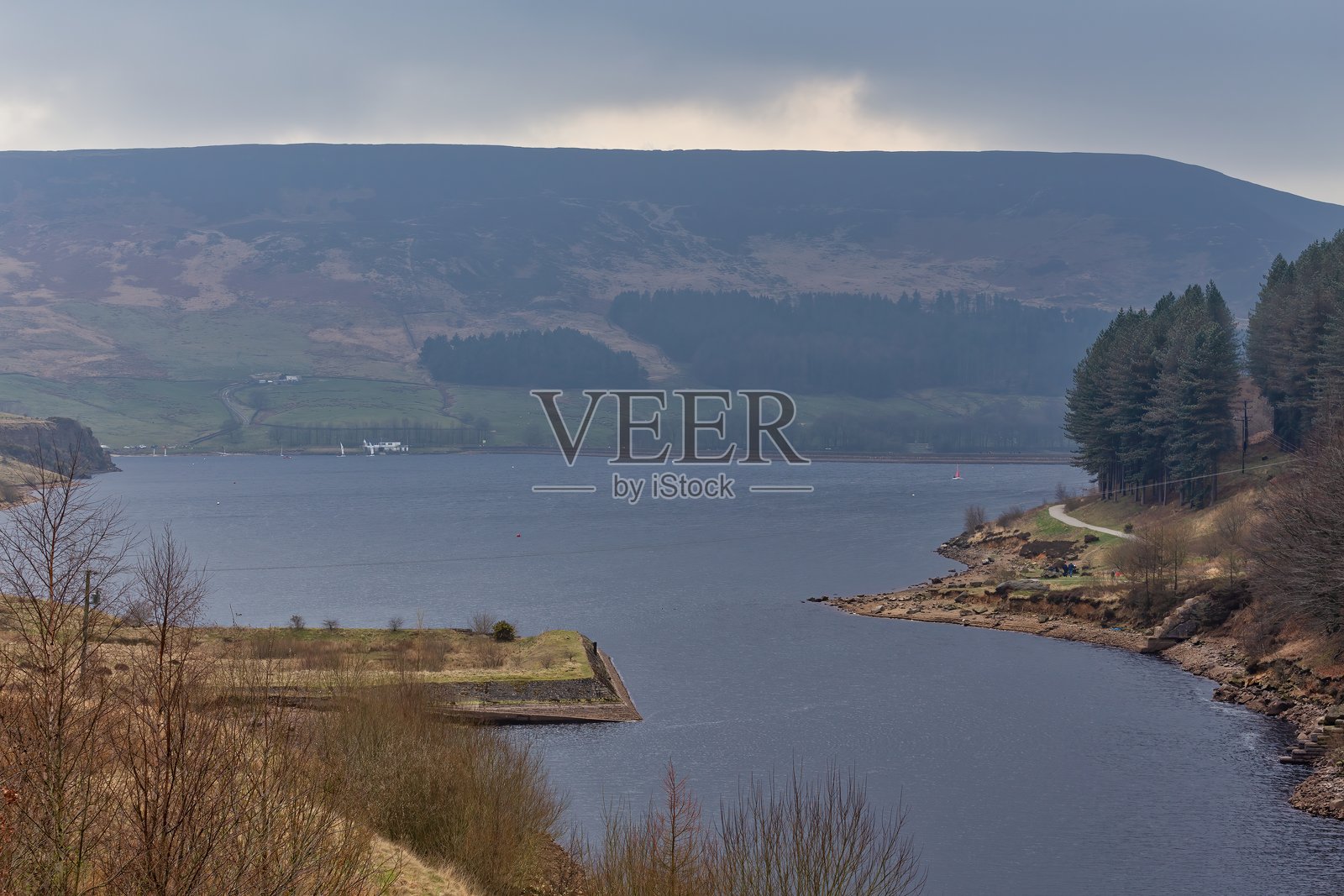 一片湖泊坐落在起伏的山丘之间,映衬着多云的天空。照片摄影图片