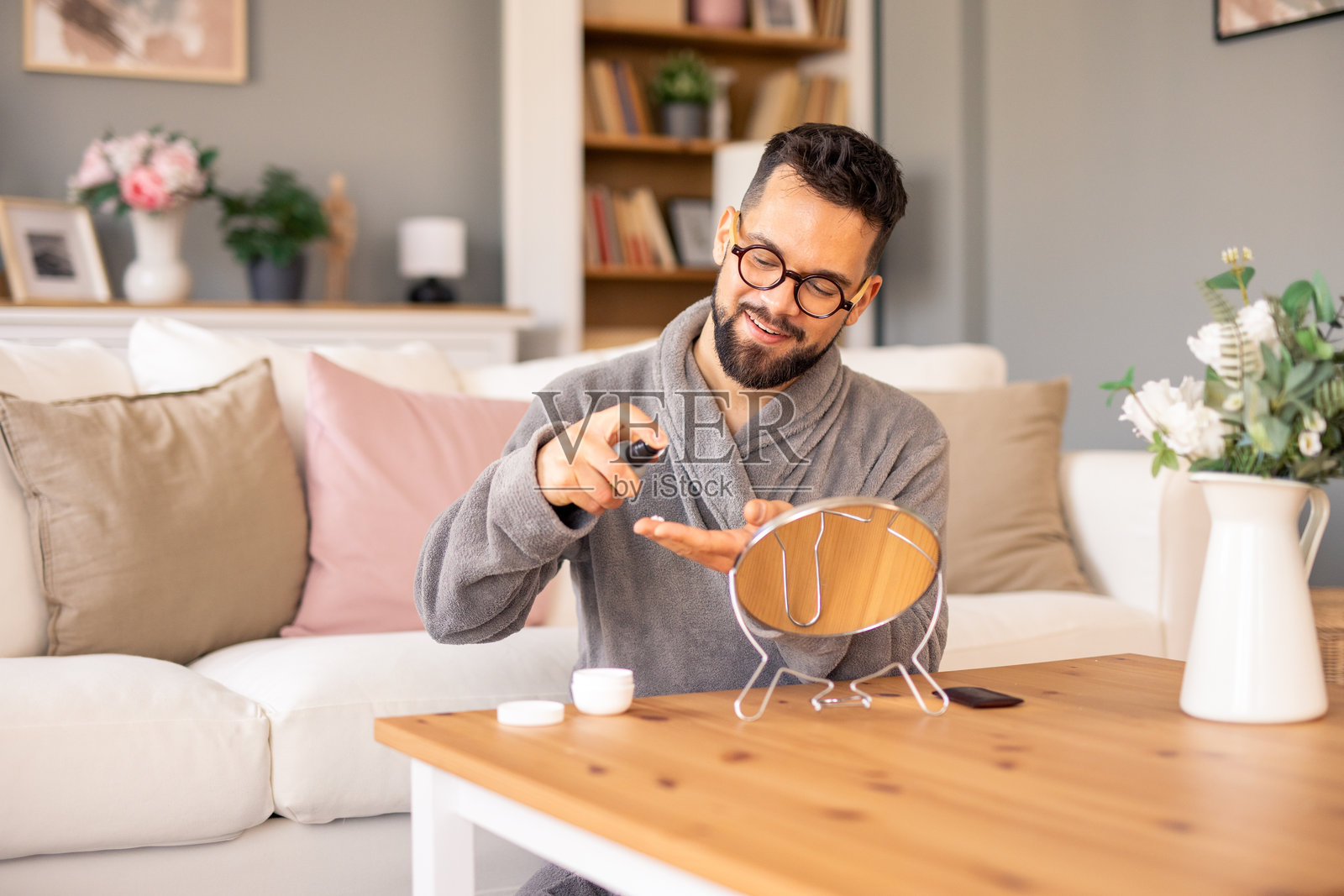 微笑的白人男性穿着灰色长袍,在舒适的客厅里涂抹面霜照片摄影图片