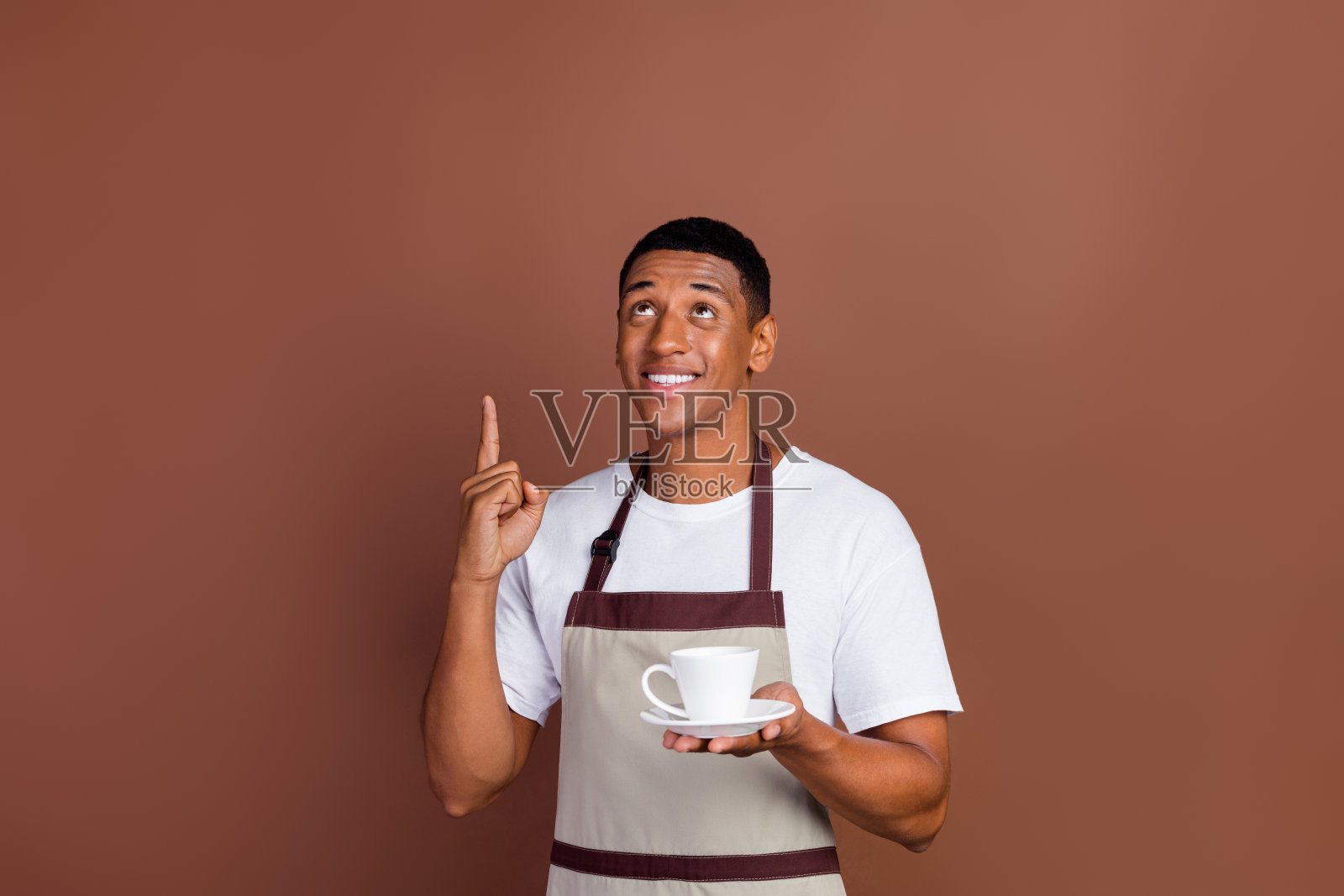 年轻的非洲裔男子手持杯子,指向空白区域,适合广告宣传,背景为棕色。照片摄影图片