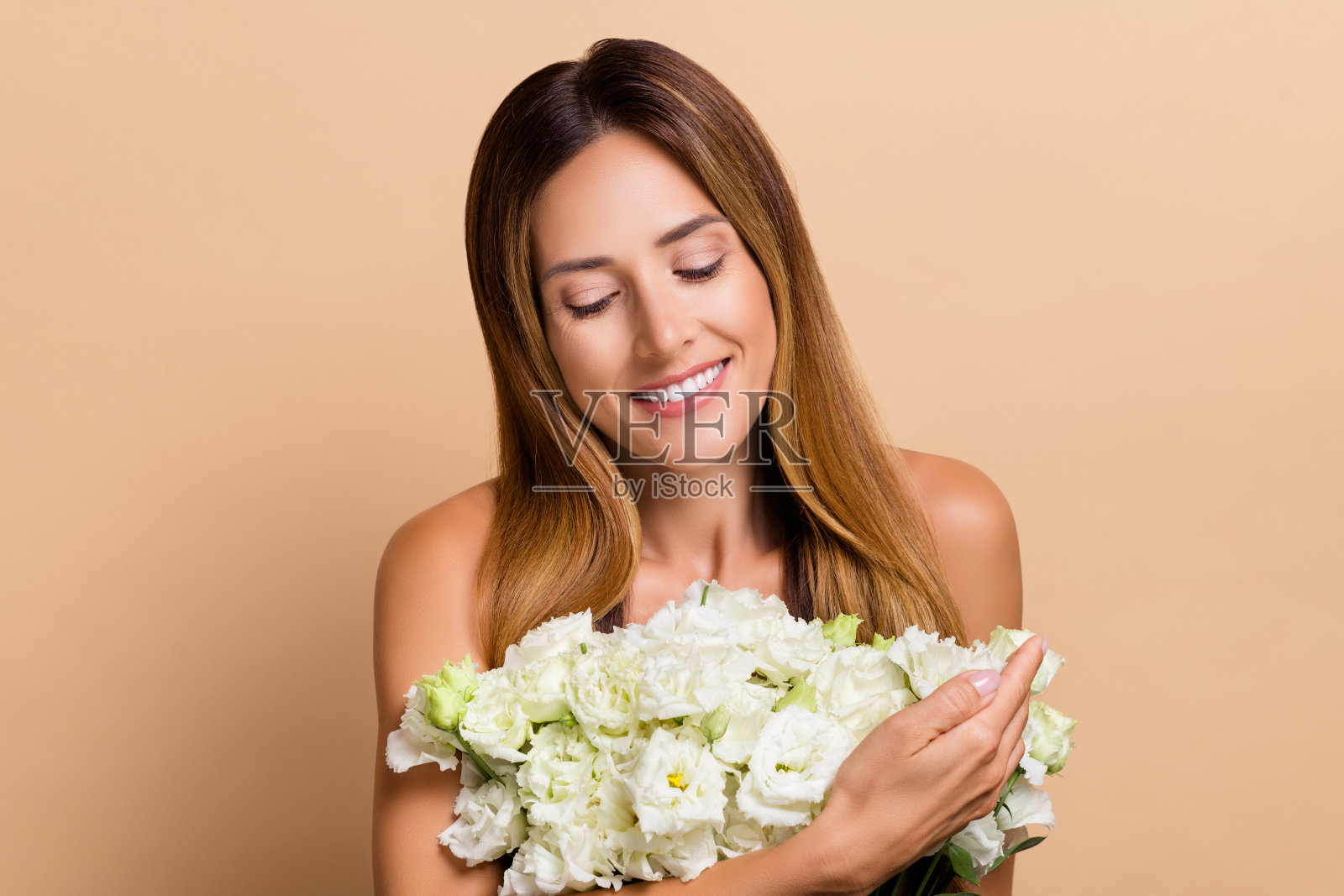 迷人、愉快、梦幻的女性手捧新鲜浪漫的玫瑰,闻着花香,背景为米色柔和色调。照片摄影图片