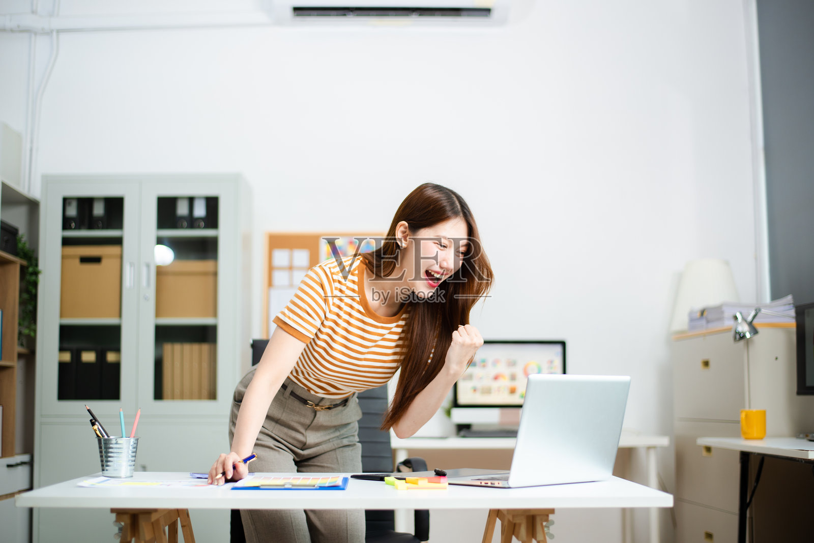快乐的女商人因收到好消息或取得成功而在笔记本电脑前欢呼。照片摄影图片