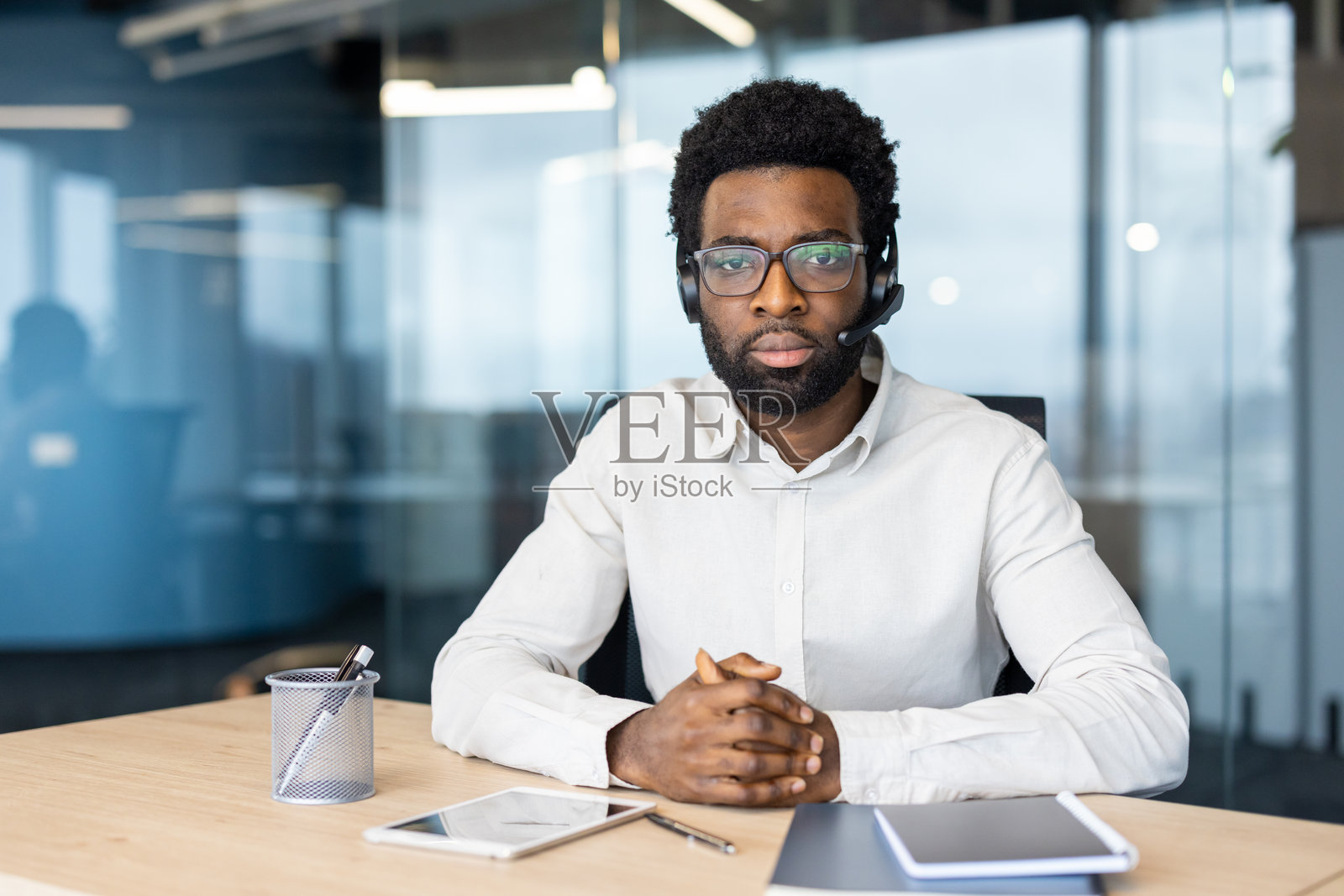 一位专注的黑人男性,戴着耳机和眼镜,身处办公室环境,准备为客户提供帮助。照片摄影图片