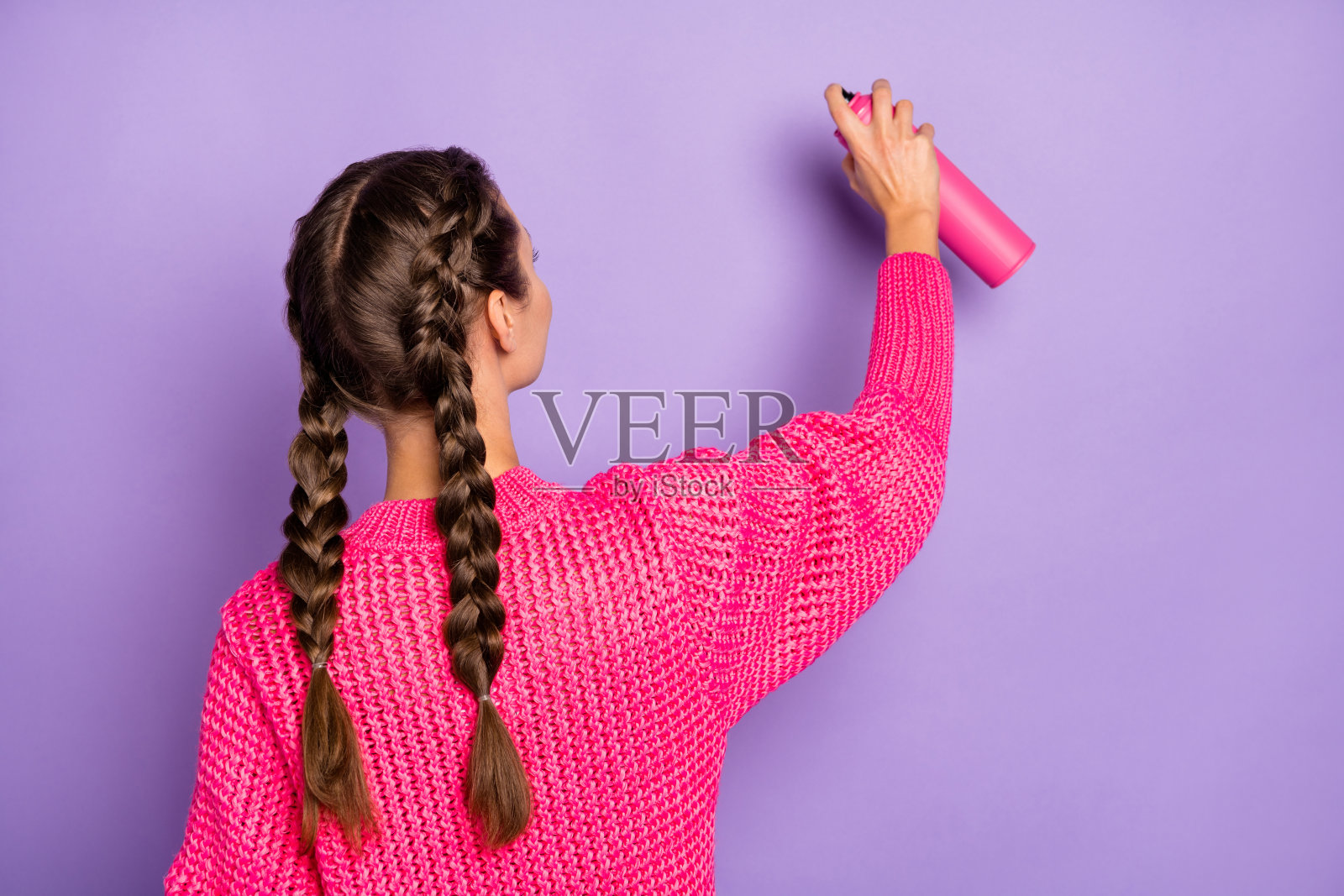 年轻女性从背后视角手持喷漆在墙上创作,背景为紫色。照片摄影图片