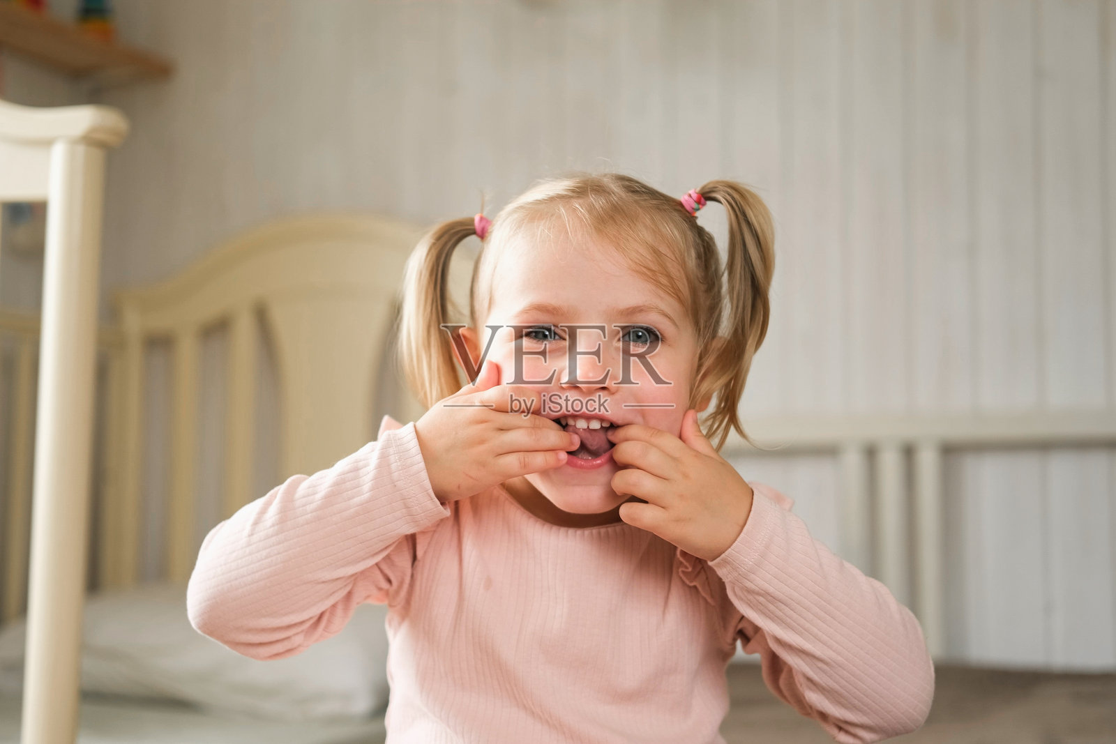 小女孩做鬼脸,吐舌头,表情搞笑。孩子在做面部表情。可爱的白人女孩在卧室里笑得很开心,做出疯狂搞笑的姿势。照片摄影图片