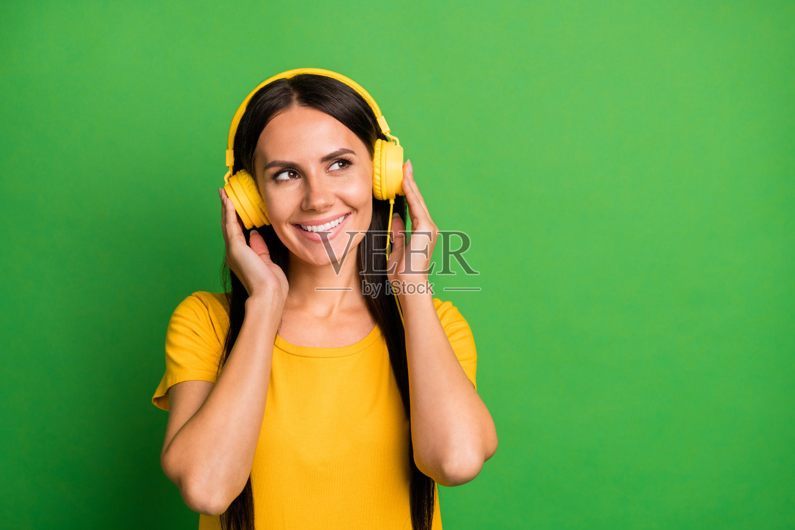 迷人的梦幻女性在鲜艳的绿色背景下享受音乐,佩戴耳机。照片摄影图片