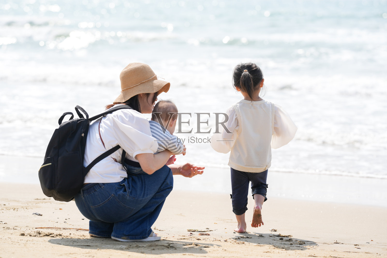 在三月初,一位1岁的日本女孩好奇地在海滩上探索,她的父母在30多岁,紧紧关注着她。这是一个温暖的春季家庭时刻,充满了亲密的连接。照片摄影图片