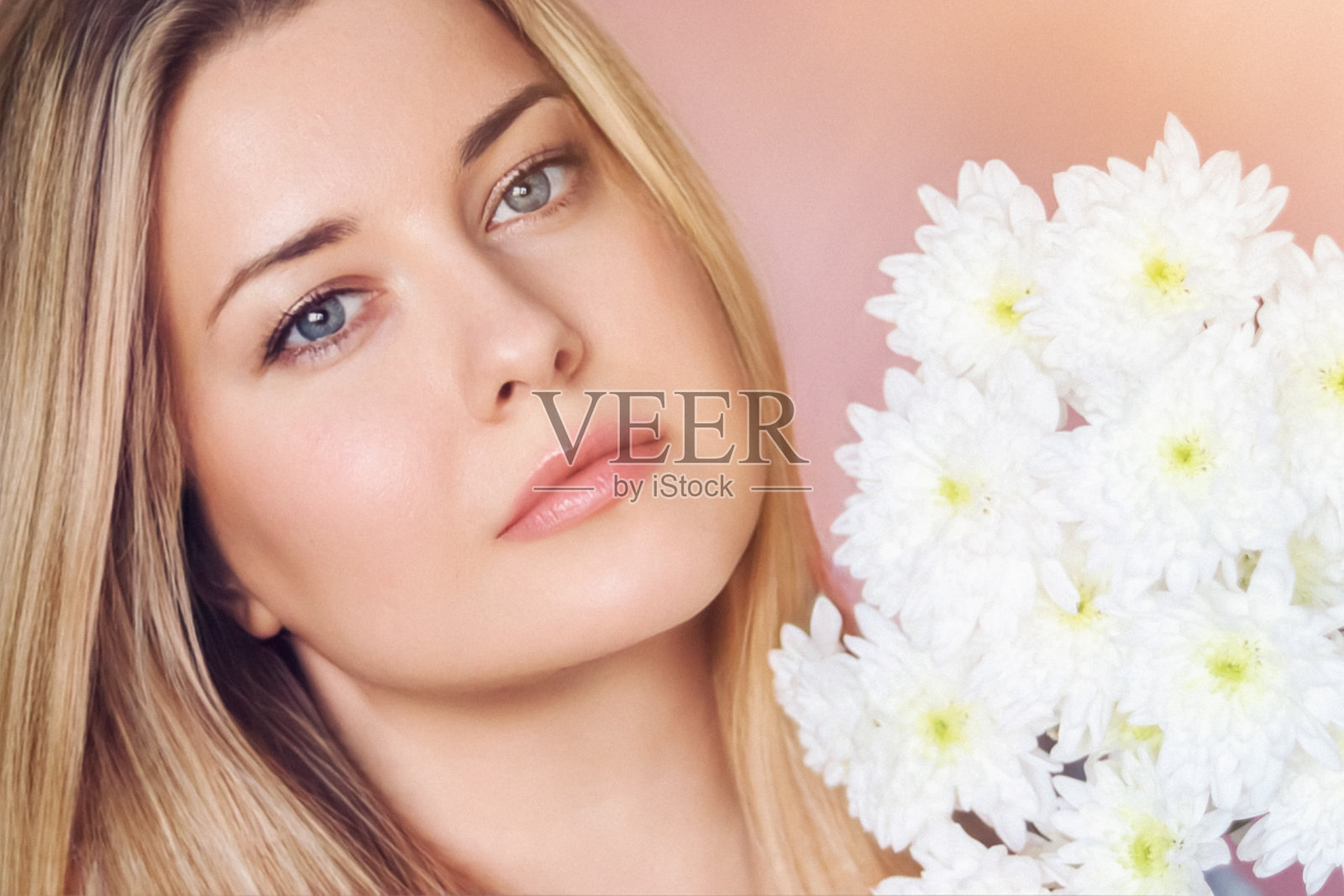 花卉之美与宁静肖像,金发碧眼的女性手捧白色菊花,柔和的粉色背景照片摄影图片