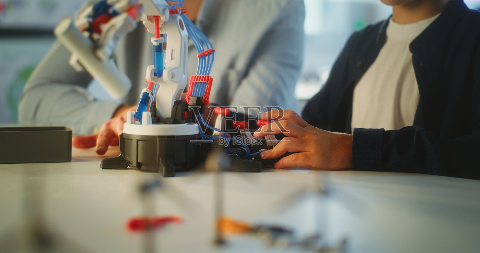 小男孩在小学与老师一起研究机器人手臂模型的特写镜头照片摄影图片