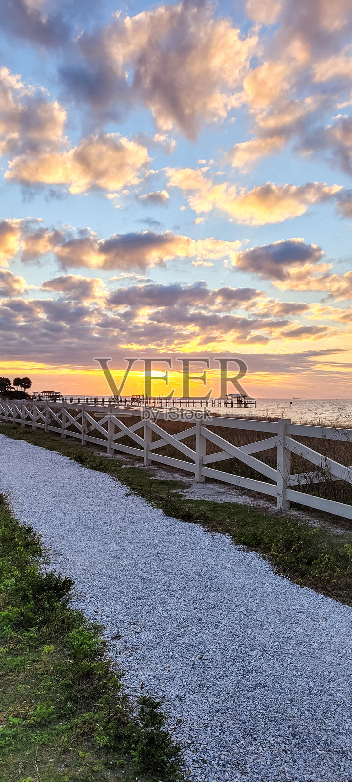 在佛罗里达州坦帕湾阿波罗海滩附近,夕阳下的直木栅栏背景中,石子小路蜿蜒而行。照片摄影图片