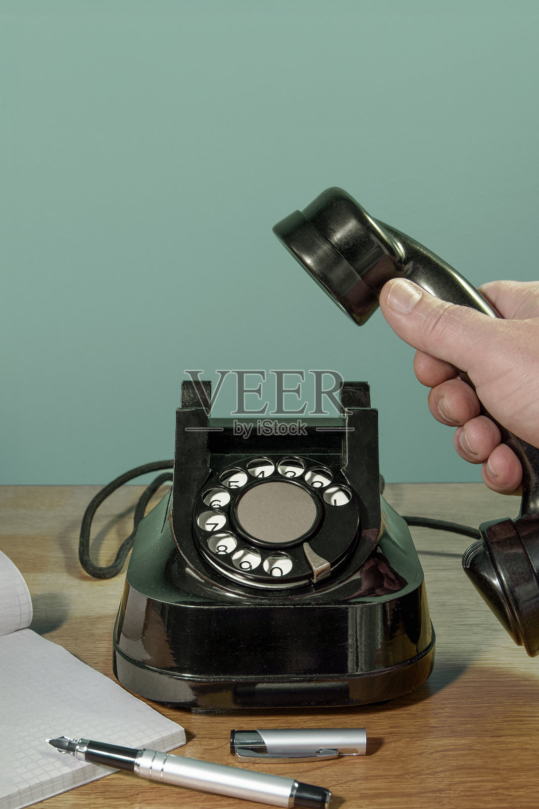 复古电话,手拿起桌面上的电话听筒,旁边有一本笔记本和一支笔。绿色背景的竖幅横幅。照片摄影图片