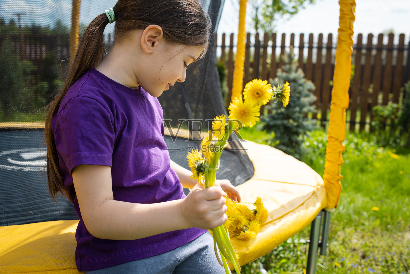 夏季假期在大自然中。孩子坐在后院的蹦床上,编织蒲公英花环,享受温暖阳光的春日。儿童夏令营。照片摄影图片