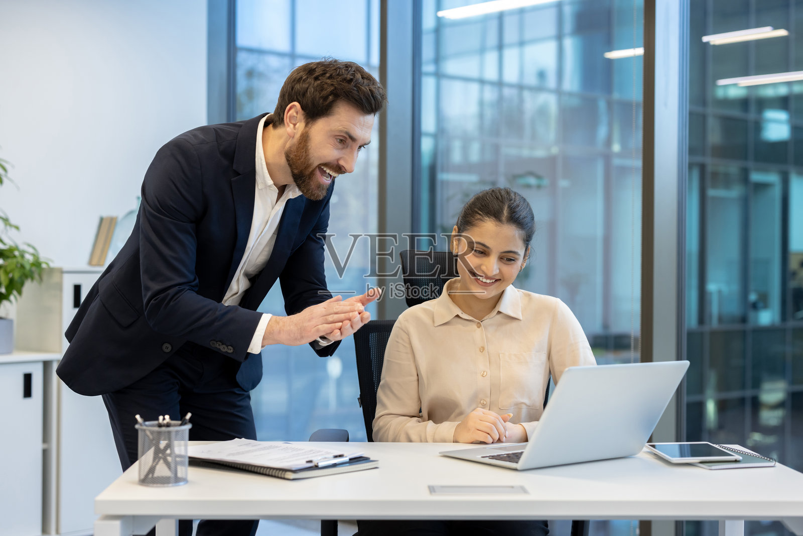 一位男商人和一位女商人在明亮的现代办公室里微笑着看着笔记本电脑。照片摄影图片