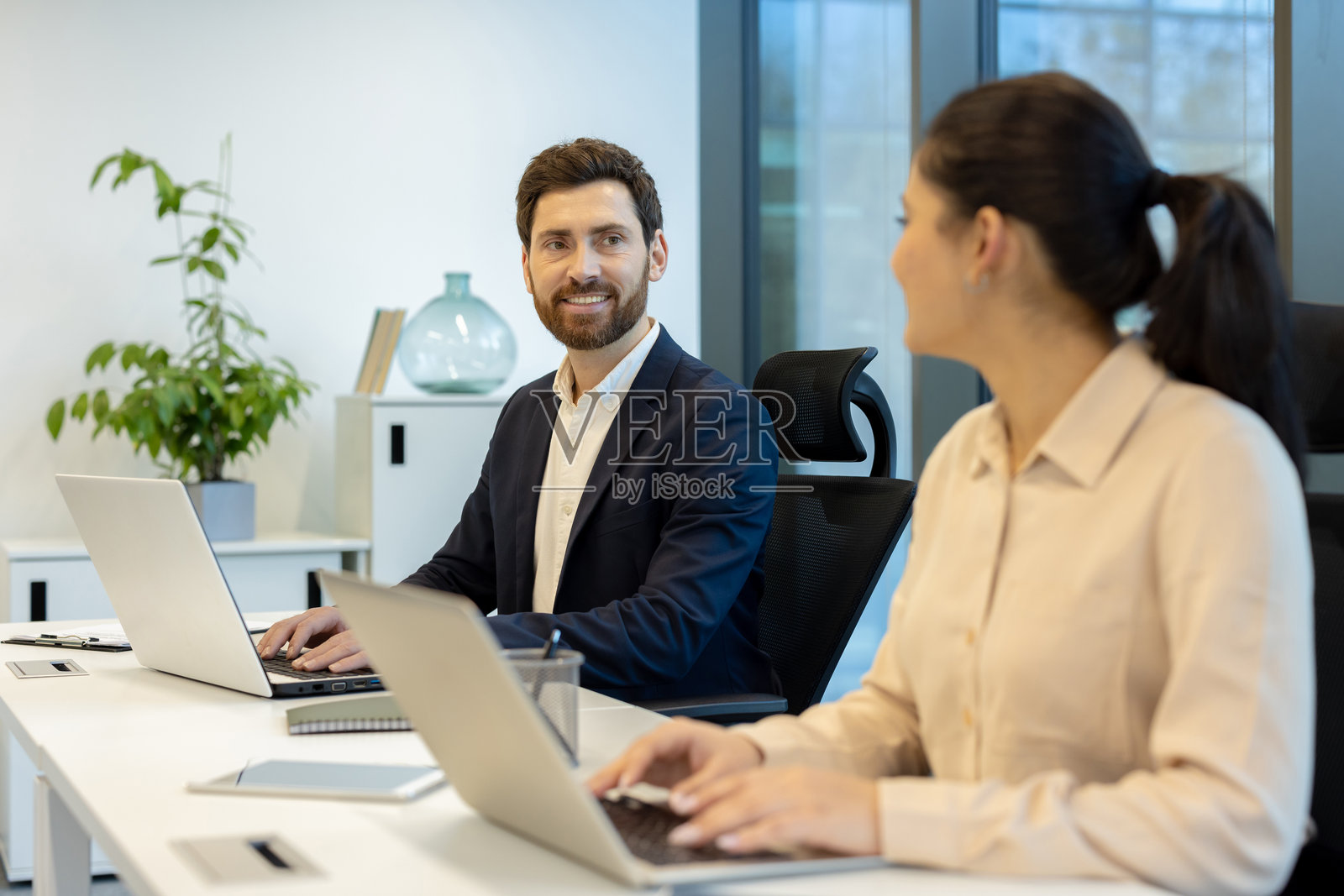 两位同事在办公室合作,一起在笔记本电脑上工作并分享想法。照片摄影图片