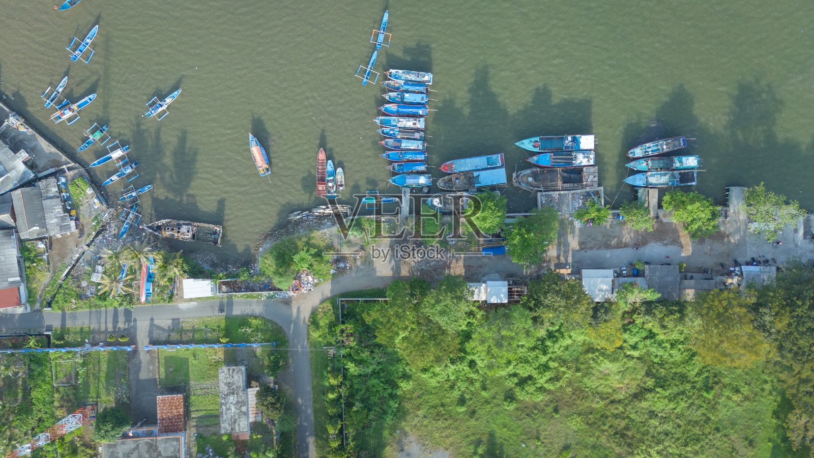 鸟瞰图展示了一个村庄的海滨,周围有许多船只和郁郁葱葱的绿树。照片摄影图片