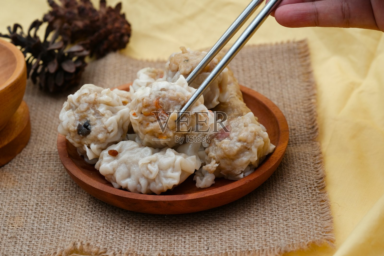 一只手用筷子夹起盘子里的点心饺子,旁边有一碟蘸酱,背景是麻布布料。照片摄影图片