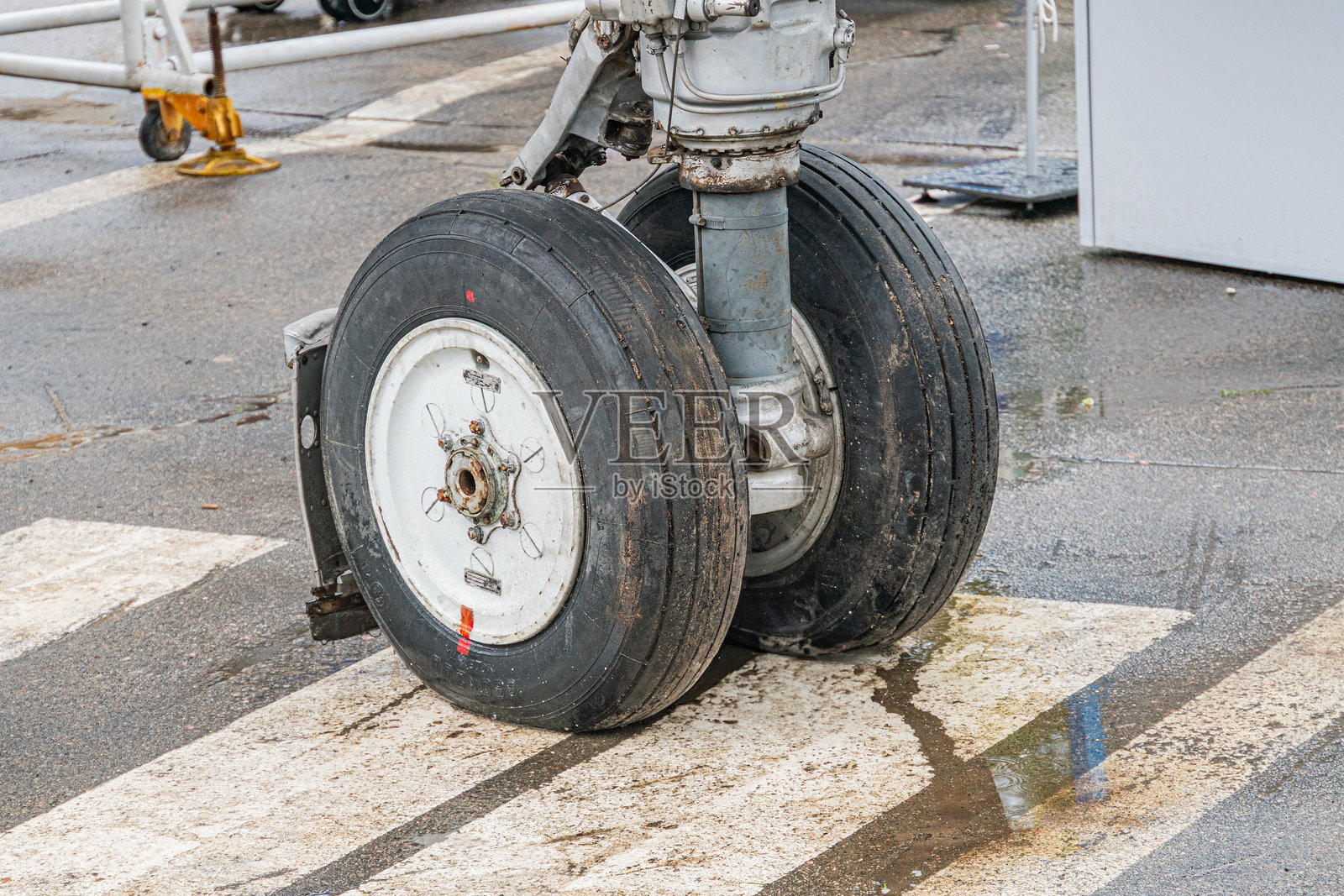 一架喷气式飞机停在机场跑道上,配有两个黑色轮胎和散落的水洼,自然的漫射光照,地球色调主导场景,跑道上标有白色线条,抓拍风格的照片。照片摄影图片