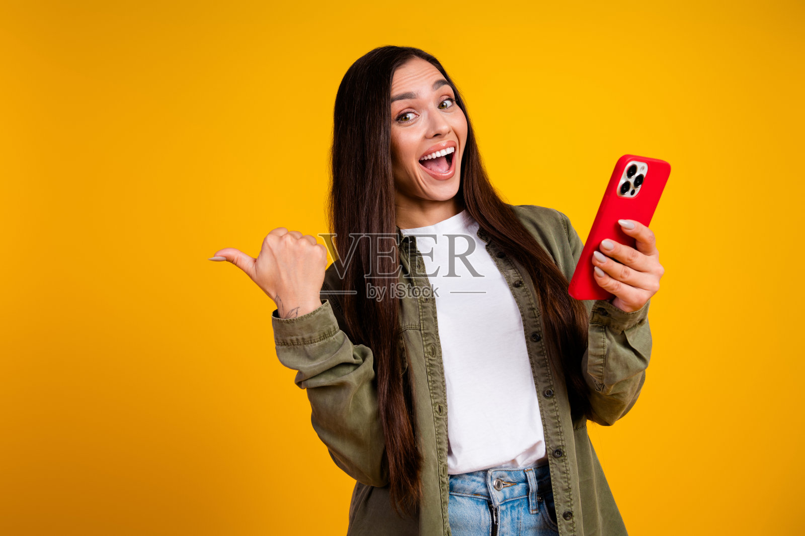 愉快的年轻女性手持智能手机,在鲜艳的黄色背景前做出富有表现力的姿势照片摄影图片