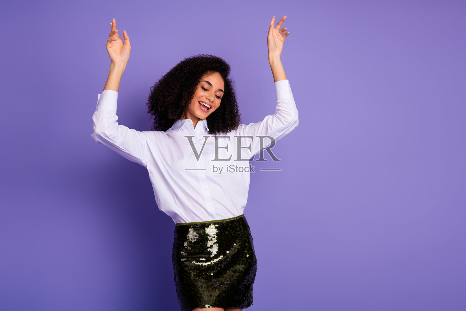 穿着时尚正式服装的年轻女性在紫色背景前摆姿势,双臂高举,散发出自信气息照片摄影图片