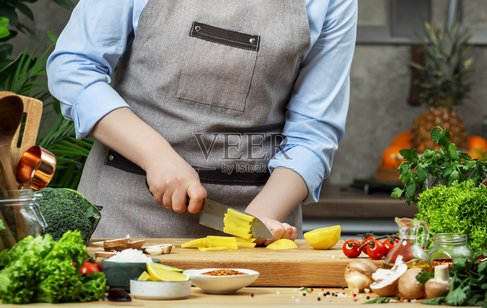 厨师在厨房烹饪食物。厨师将土豆切成条以制作薯条。木桌、厨房用具、蔬菜、香草和配料。健康的素食饮食、食谱、博客。照片摄影图片
