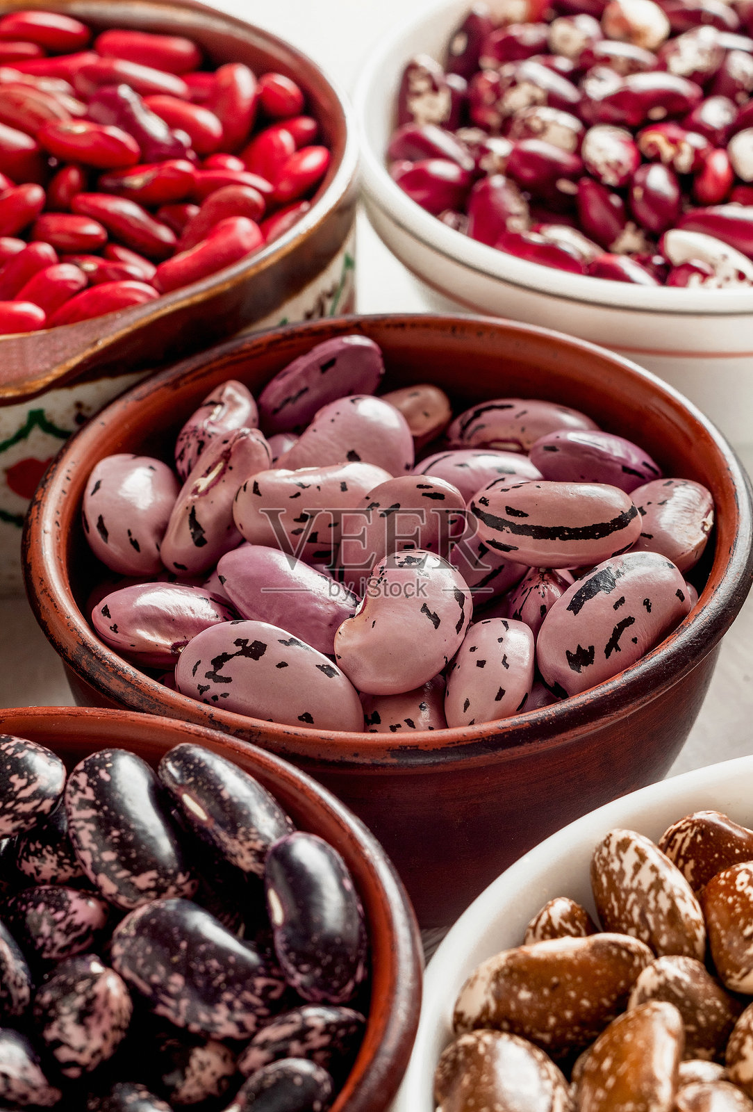 不同有机豆类的陶瓷碗。猩红跑豆、肾豆、阿纳萨齐豆、斑点豆。富含蛋白质的植物食品。照片摄影图片