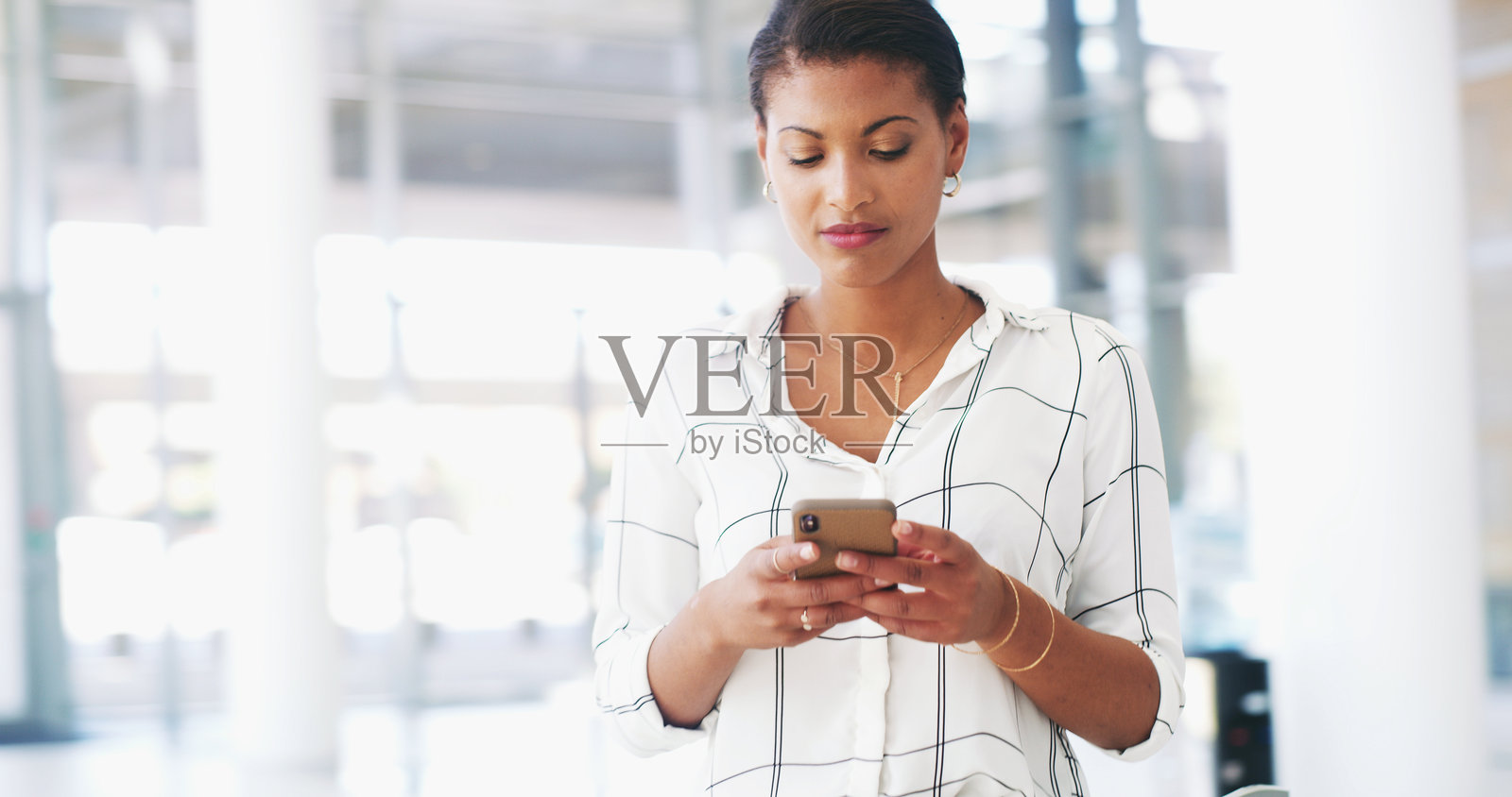 在办公室里,商务女性正在打字、使用手机,并接收在线通知、信息和网络消息。专业的企业员工在大厅中使用智能手机进行社交媒体、沟通和B2B联系。照片摄影图片