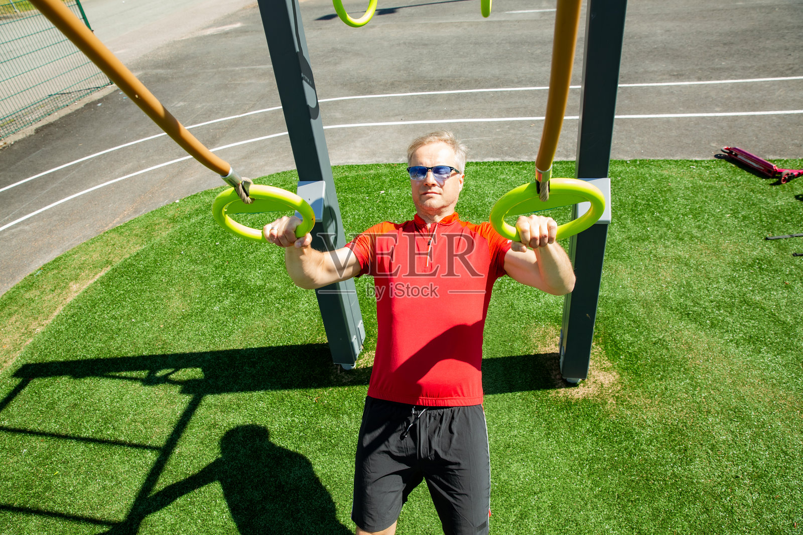 中年男子在户外健身公园的体操环上进行自重划船训练。功能性锻炼增强上半身力量。照片摄影图片