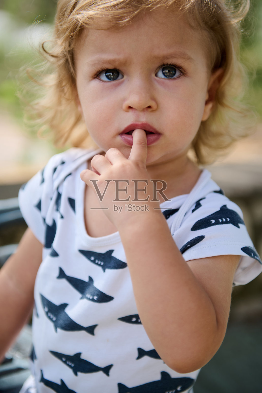 好奇的小孩在户外穿着鲨鱼图案的衬衫,手指放在嘴唇上。照片摄影图片