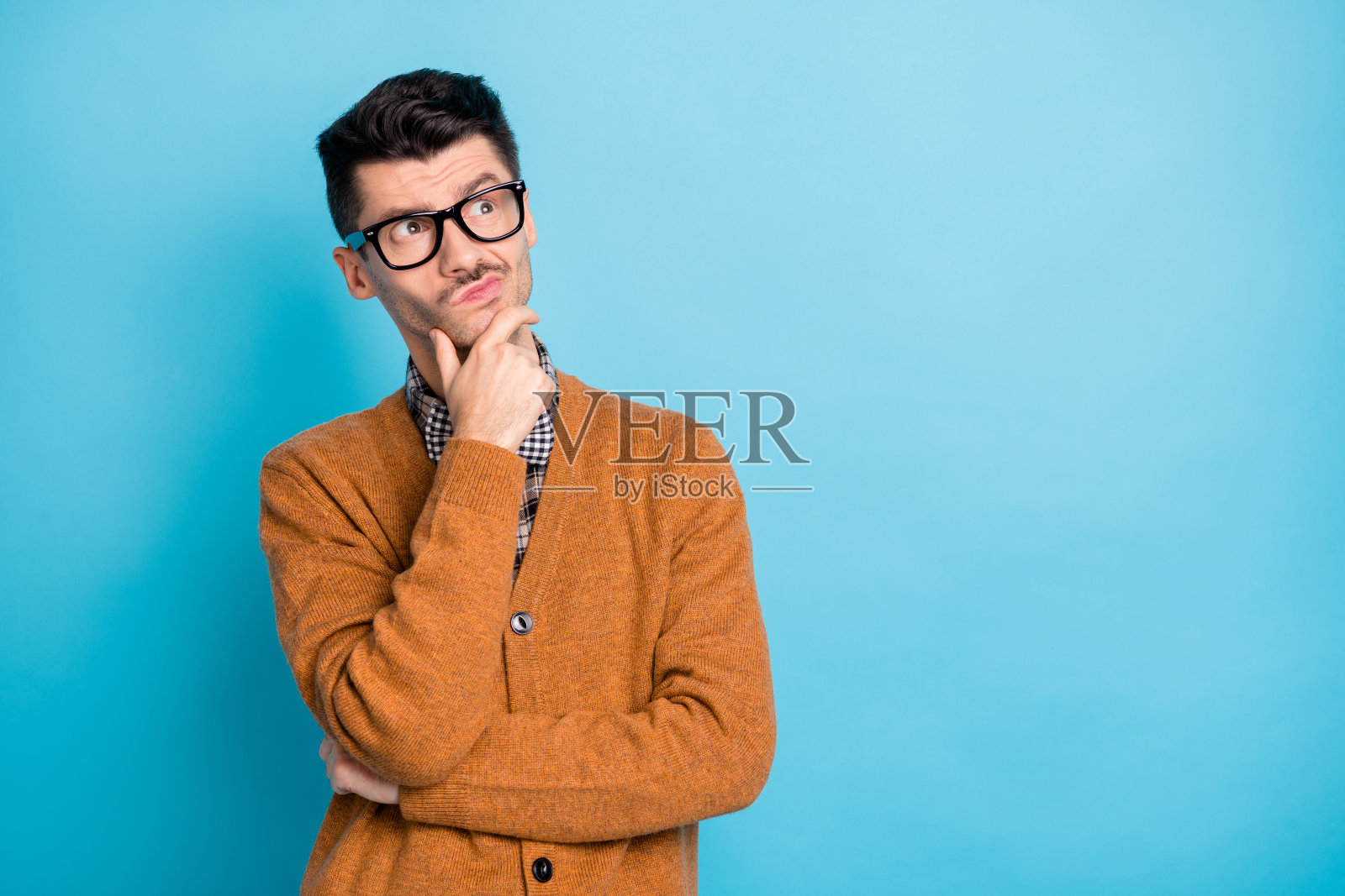 沉思的帅气年轻男子托着下巴,凝视空旷的空间,梦想着,背景为蓝色。照片摄影图片