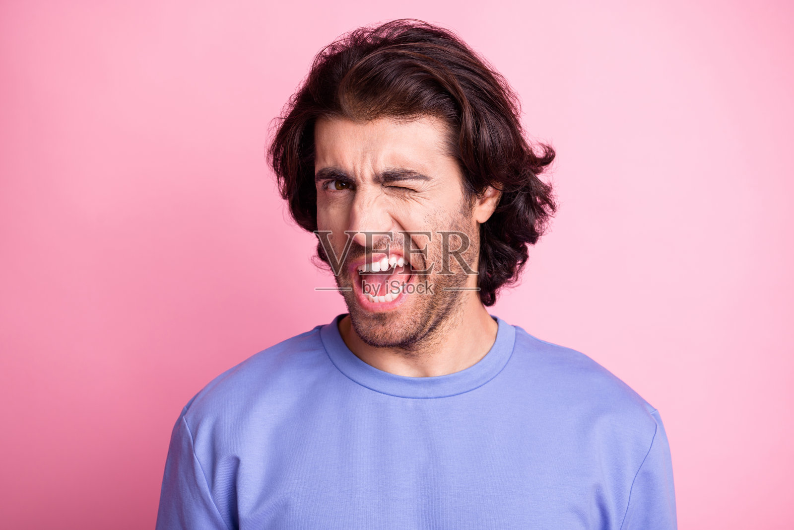 迷人、开朗、帅气的男人眨眼,穿着紫色毛衣,背景为柔和的粉色光泽。照片摄影图片