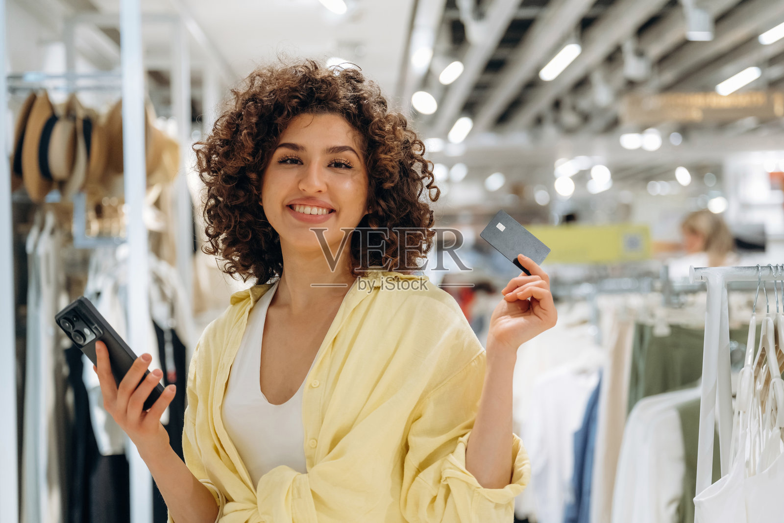 卷发、微笑、信用卡和智能手机。女人在服装店购物。照片摄影图片