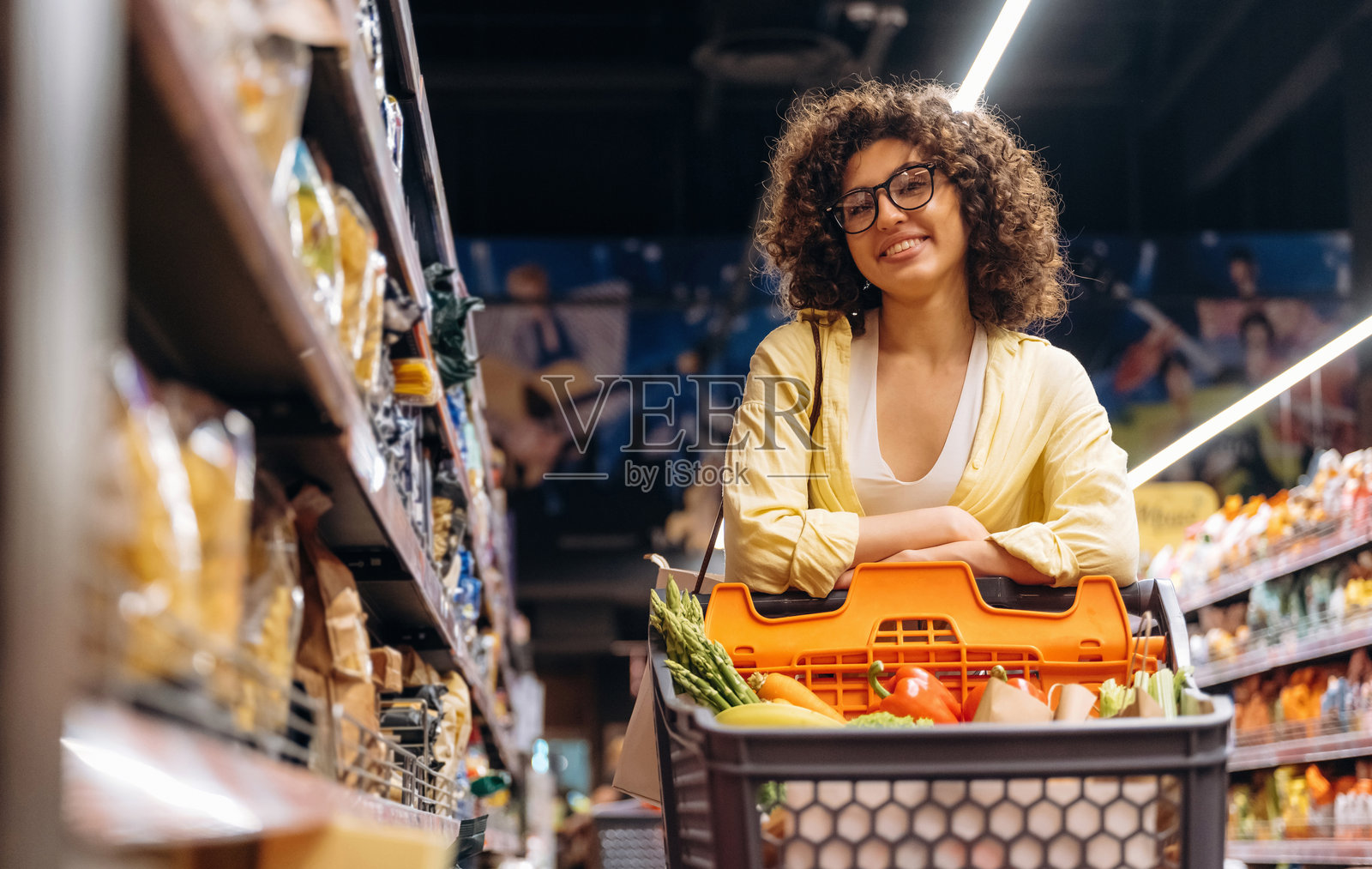在货架旁边的产品前。一位美丽的女性在杂货店里。照片摄影图片