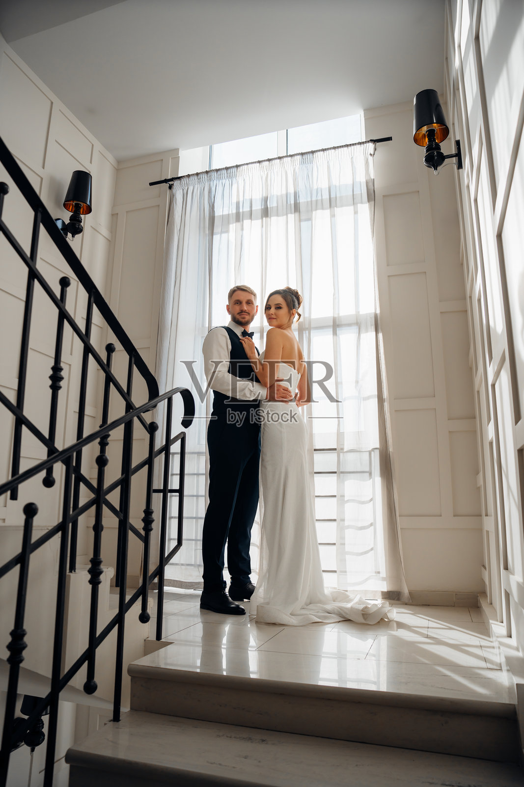 美丽的新郎和新娘在楼梯上与大窗户合影照片摄影图片
