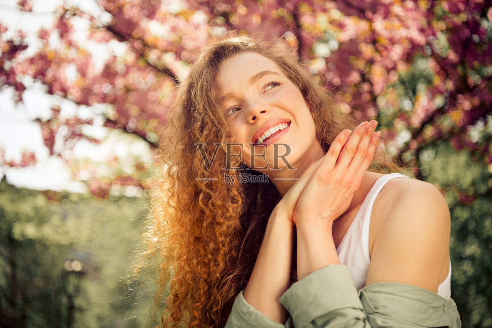 可爱的年轻女性,卷曲的红发,在春天的花园中微笑,周围是五彩缤纷的花朵。照片摄影图片