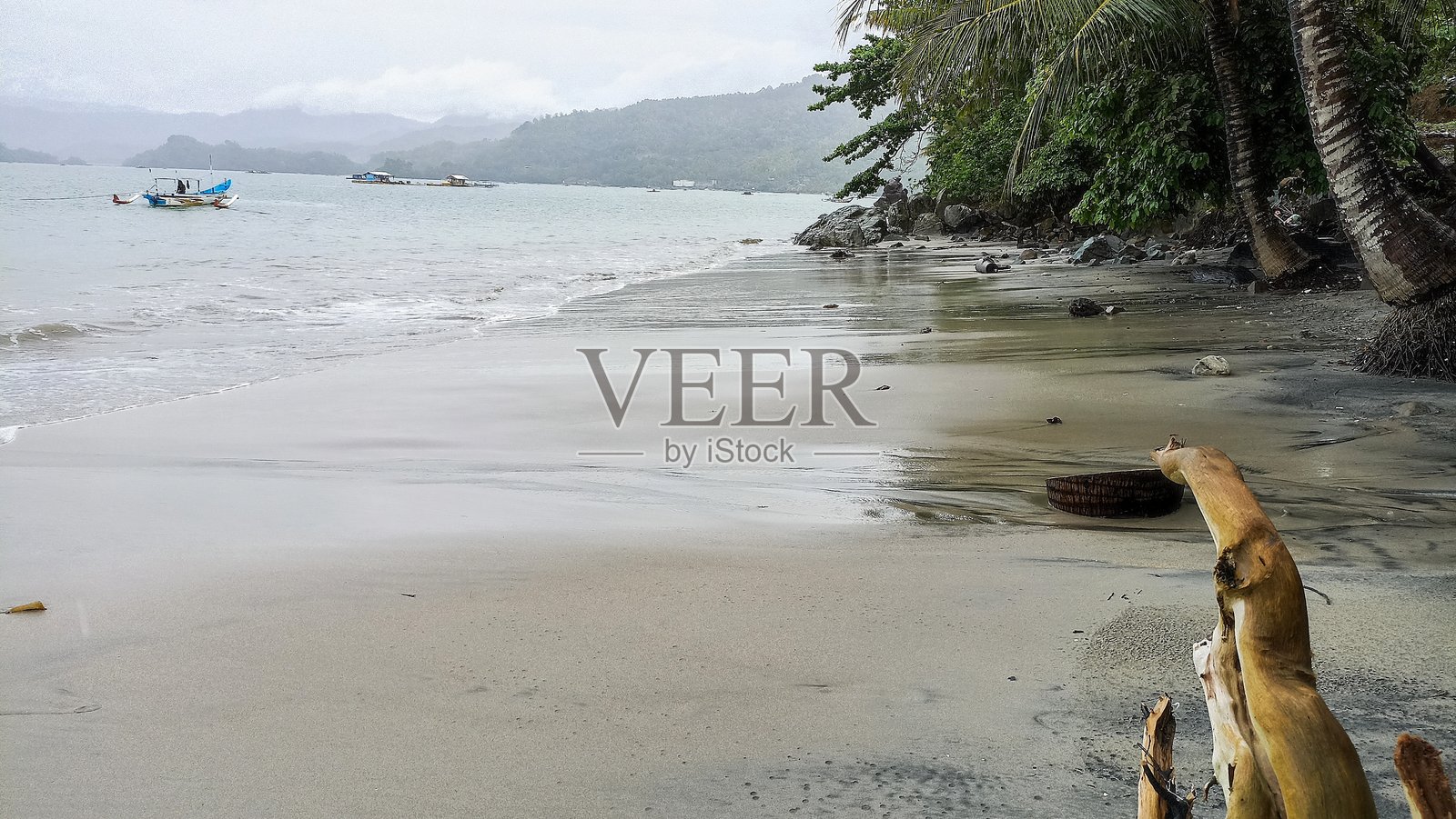 宁静的海景,展现了一个平静的沙滩,湿润的沙子反射着阴云密布的天空,船只轻轻停靠在平静的水面上。照片摄影图片