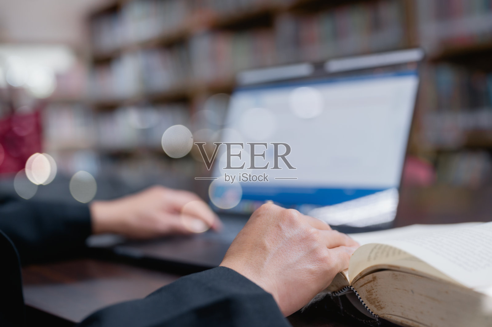 专注学习的人在安静的书桌上进行深入研究,手准备好翻阅图书,旁边有打开的笔记本电脑,身处图书馆环境中。照片摄影图片