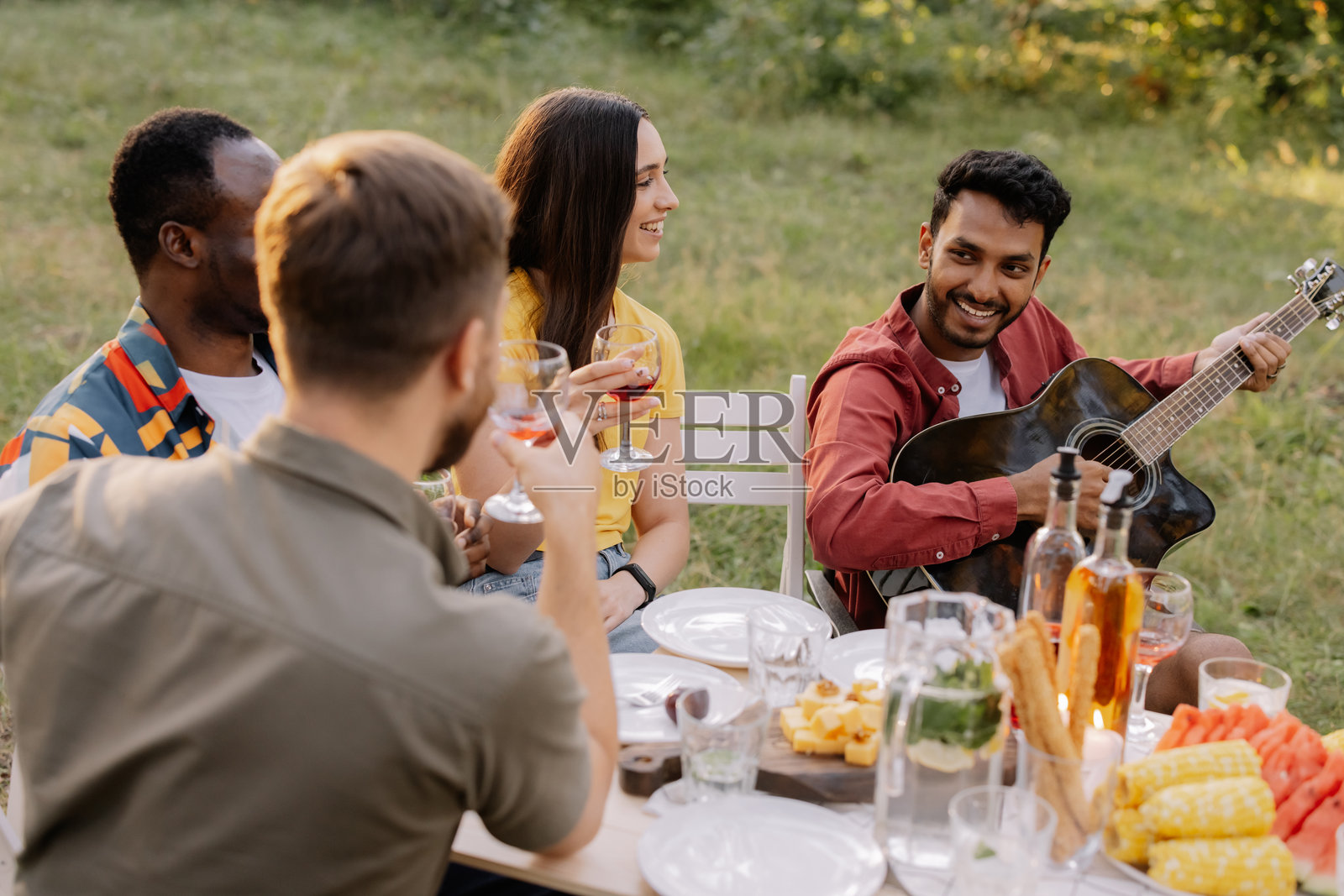 多元化的朋友们在公园里享受音乐和葡萄酒的野餐照片摄影图片