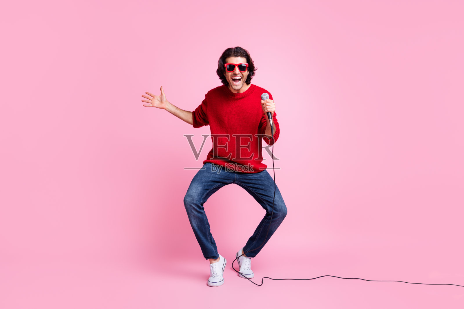 手持麦克风、戴着太阳镜的跳舞歌手肖像,背景为柔和的粉色。照片摄影图片