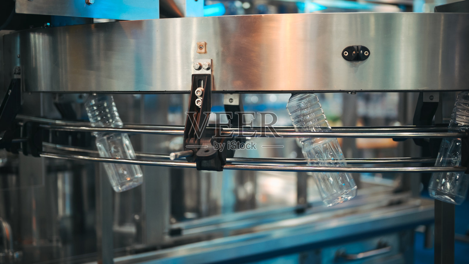 高精度灌装设备,配有透明液体容器,高容量瓶装和封盖机,位于工业自动化生产线中,具有同步多步骤工艺的包装系统。照片摄影图片