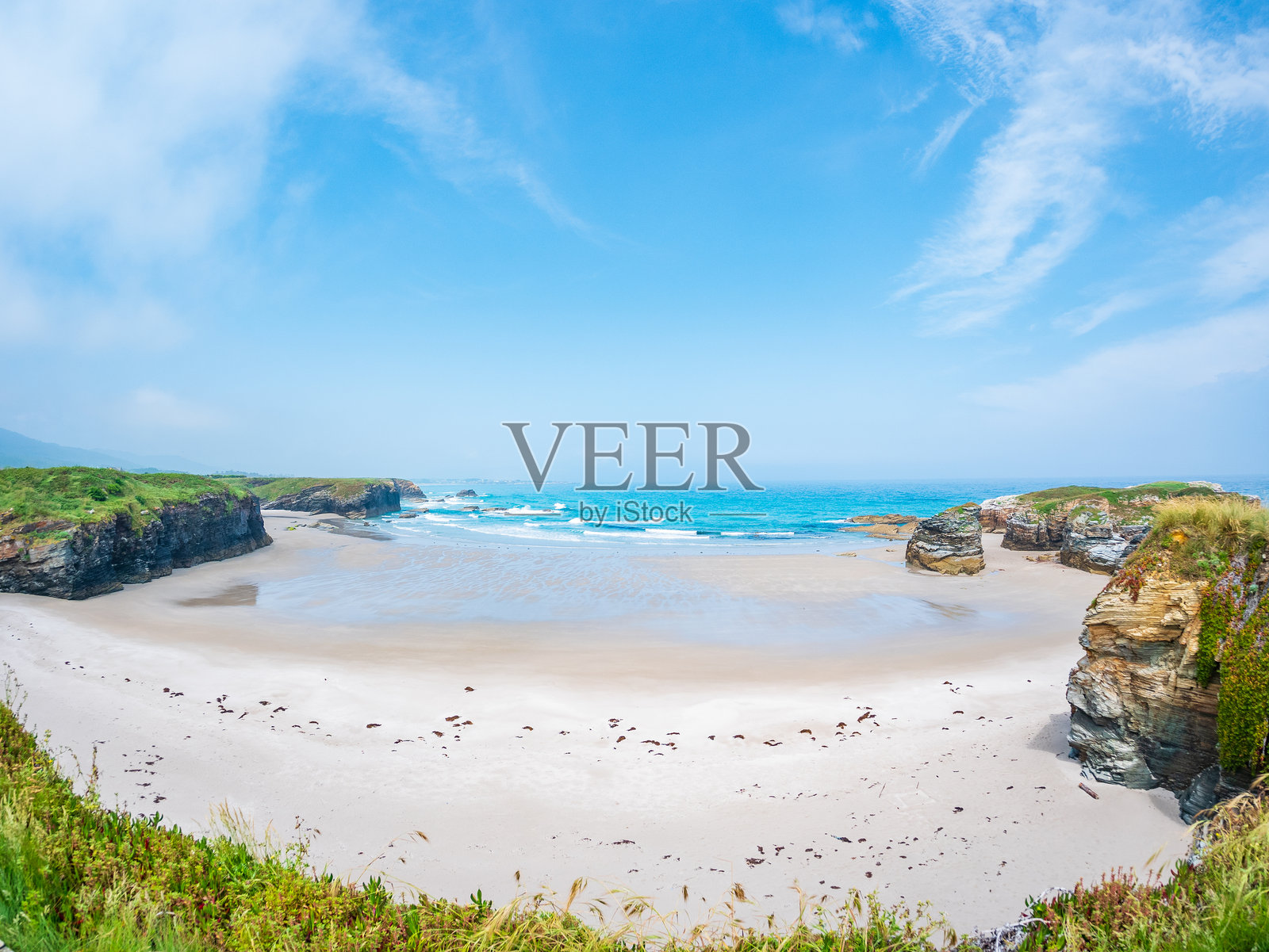 西班牙加利西亚的阿斯卡特德拉斯海滩在低潮时显露出沙岩、潮池,映照着天空,悬崖沿着宽阔的海岸线,在明亮的光线下展现出宁静的自然奇观。照片摄影图片