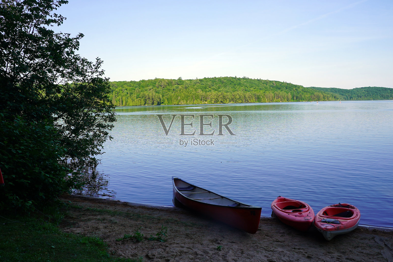 一只红色独木舟和两只红色皮划艇静静地停在沙滩湖岸上照片摄影图片