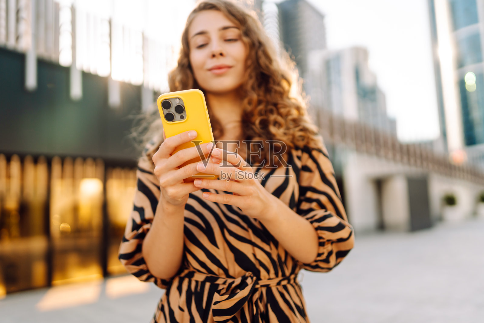 一位年轻女性手持黄色手机,背景是城市大都会的特写镜头。照片摄影图片