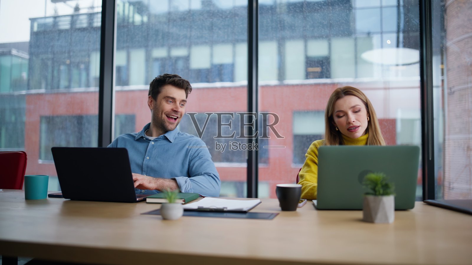 微笑的同事在工作场所交谈,特写镜头。男人在看女人的笔记本电脑。照片摄影图片