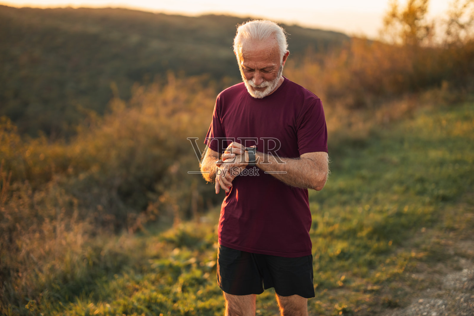 老年男子在日落时分户外散步时查看健身手表照片摄影图片